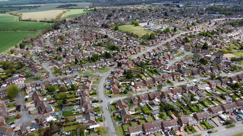 An aerial view of a suburban residential area featuring a set of railway tracks running vertically through the center of the image. On either side of the tracks are rows of detached and semi-detached